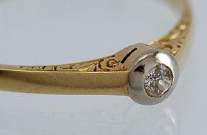 Prsten ze zlata ryzosti 585/1000 (14 kart), briliant velikosti 0,05 ct, prce ze 30. let 20. stol. s peliv provedenou rytinou u hlavy prstenu. Samotn kmen zasazen v blm zlat.